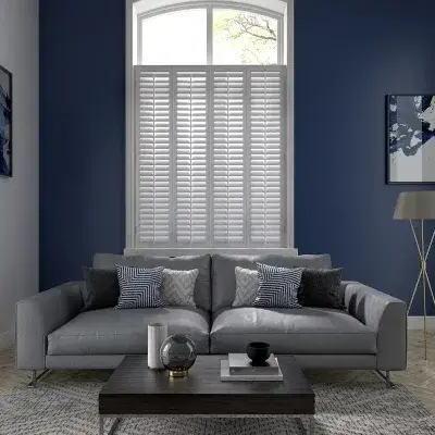 White shutters on a tall window behind a sofa